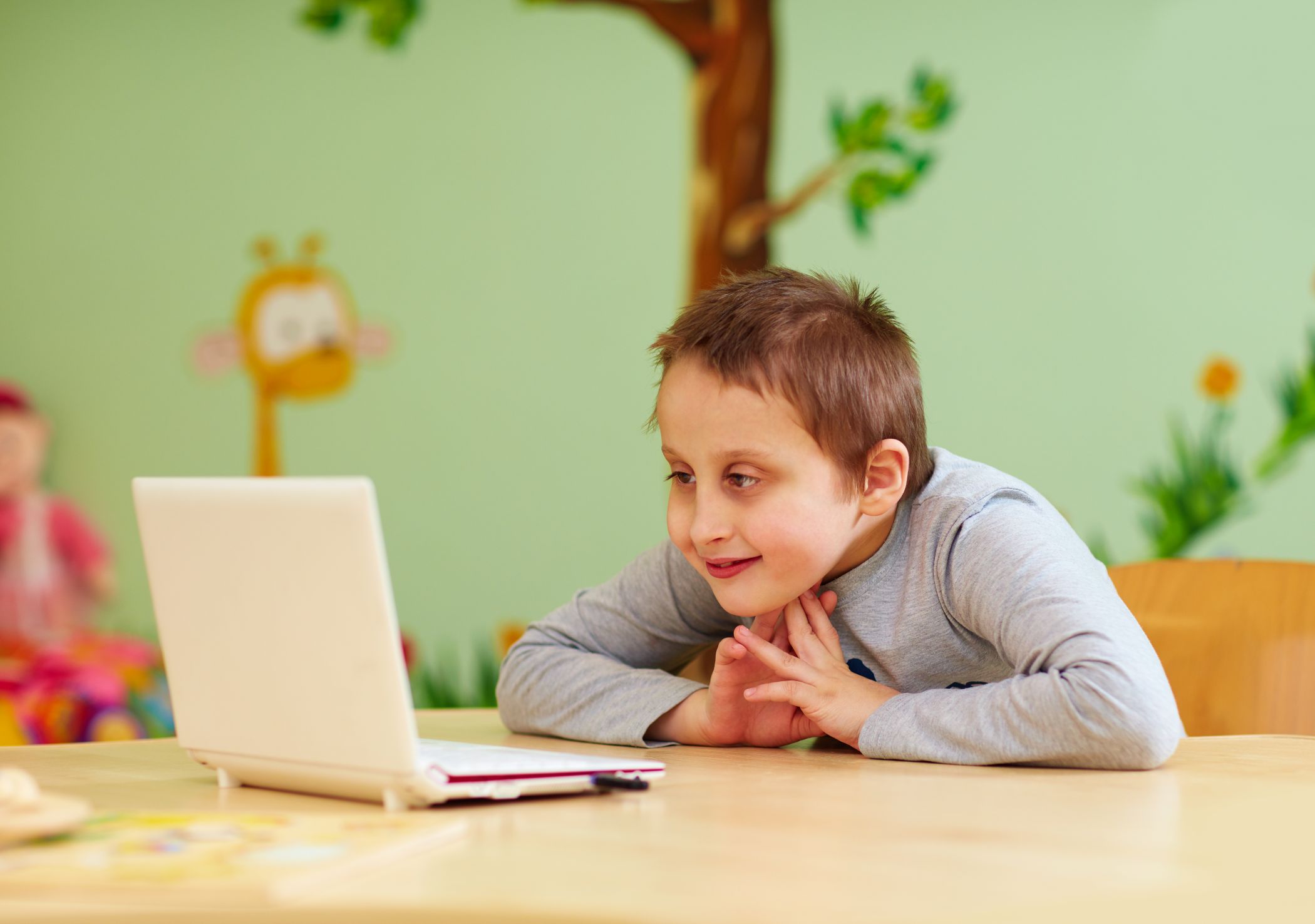 Young boy with special needs watching media through a laptop at school.